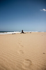 Fototapeta na wymiar a man remains silent on a tree trunk leaving footprints on the sand of the beach