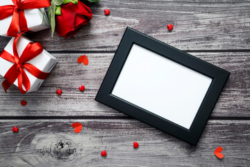 Empty black frame mock up with red rose, gift box and heart on old wood. Top view valentine, wedding and love.
