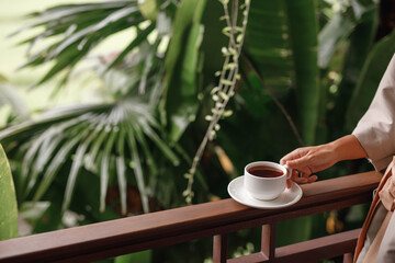 Woman holding cup of hot steaming drink tea on the  balcony with tropical view