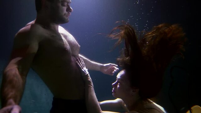 A passionate and beautiful couple, a man and a woman swim together under the water, move beautifully, they have passion.