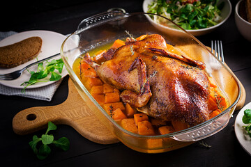 Homemade baked duck. Crispy whole roast duck. Thanksgiving or Christmas dinner. Roast duck with thyme and pumpkin on rustic wooden table.