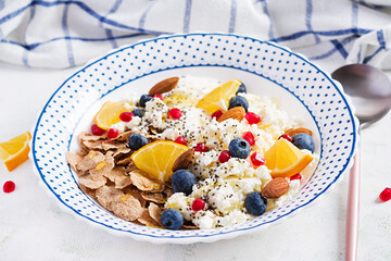 Bowl of flakes with cottage cheese and yogurt, blueberryes and pomegranate on white table. Fitness food.