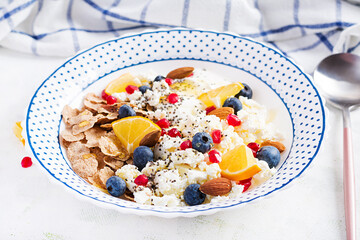 Bowl of flakes with cottage cheese and yogurt, blueberryes and pomegranate on white table. Fitness food.