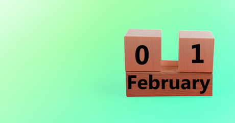 Wooden block calendar with the date February 01 on a green gradient holiday background with a copy of the space and space for your text