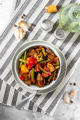 Pickled vegetables in a gray bowl on the light gray kitchen table. Different vegetables - red pepper, eggplant, carrots and peas in a bowl. Vegetarian dish