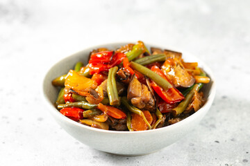 Pickled vegetables in a gray bowl on the light gray kitchen table. Different vegetables - red pepper, eggplant, carrots and peas in a bowl. Vegetarian dish