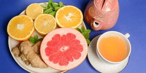 Tea cup and tea pot with cut citrus fruit over blue background. Tea time, healthy lemon and grapefruit drink concept.