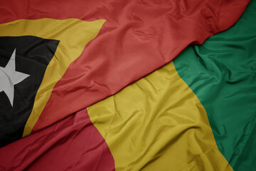 waving colorful flag of guinea and national flag of east timor.