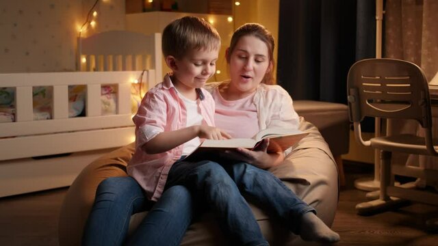 Slow motion of young mother reading bedtime story to her little son before going to sleep. Concept of child education and family having time together at night