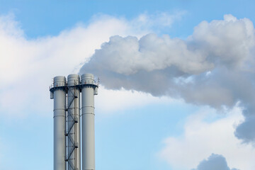 Emissions of smoke and steam from an industrial chimney into a clear sky.