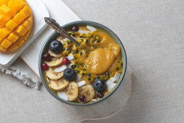 Smoothie bowl of fresh organic tropical fruits: mango, banana, passion fruit and garnished with blueberries, coconut chips