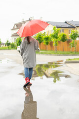 A woman with a red umbrella walks in the park in the autumn. Happy smiling multiracial girl walks cheerfully with a red umbrella down the street in the park, goes to the house