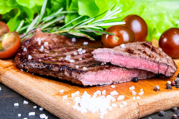 black angus steak with tomatoes, rosemary and lettuce on a board