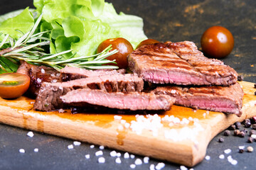 black angus steak with tomatoes, rosemary and lettuce on a board