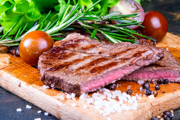black angus steak with tomatoes, rosemary and lettuce on a board