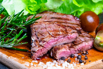black angus steak with tomatoes, rosemary and lettuce on a board