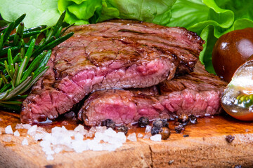 black angus steak with tomatoes, rosemary and lettuce on a board