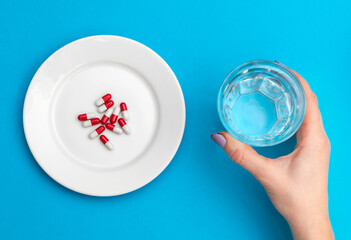 Woman's hand holding glass of water and plate with pills on blue. Medical concept. Take medication. Diet and healthy lifestyle concept.
