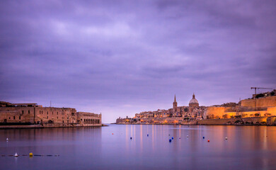 sunset on the city of valletta, malta with purple cloudy sky and ancient buildings in the background