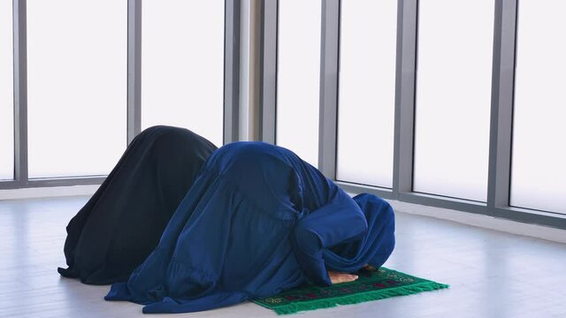 Two Asian Muslim young women in traditional hijab are praying glorify Allah and practicing the Islamic faith in mosque.