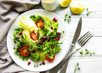 Fresh green mixed  salad bowl with tomatoes and microgreens  on white wooden background. Healthy food, top view.
