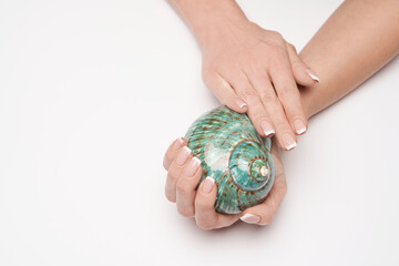 Beautiful Female well-groomed Hands with French manicure holding sea shell over light background