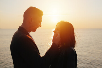 Close up portrait, the man touches with gently the woman's face. They smiling and looking each other. Happy couple at the beach on the sunset.