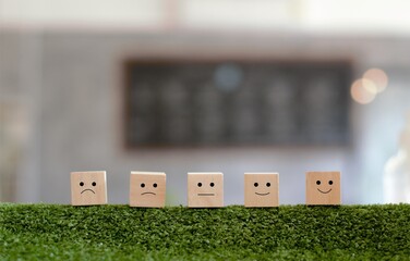 Customer satisfaction concept. Wood blocks rating with smile face on the green grass.