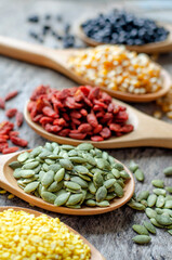Closed up dry green pumpkin seeds in wooden spoon with blur goji berry, corn, black bean and mung on grunge background