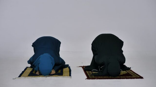 Two Asian Muslim young women in traditional hijab are praying glorify Allah and practicing the Islamic faith in mosque.