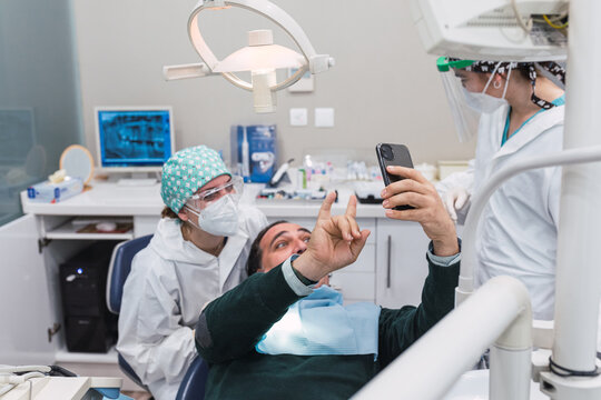 Patient taking a selfie in the dental office.Focus on the smart phone. Three people. Female doctor. Greeting and wellness concept. Smiles.