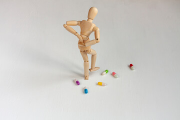 a bent wooden mannequin with back pain among colorful pills on white background