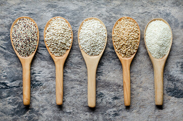 White and brown dry organnic cereal and grain seeds in wooden spoon consisted of quinoa, wheat, pearl barley, and white sesame on grunge background