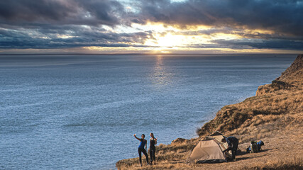 The hikers near camping tent having fun against the sea sunset background