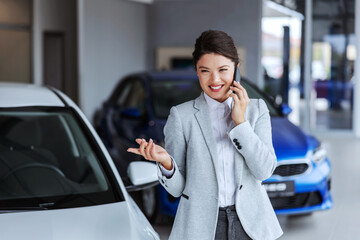 Smiling female car seller having phone conversation with a client and convincing him to buy a car....