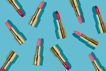 Creative pattern made with red and pink golden lipsticks on bright blue background. Retro aesthetic...