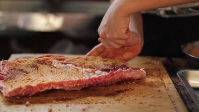 Expert chef sprinkles barbeque ingredient to pork ribs at kitchen.