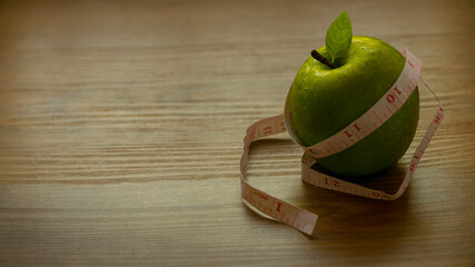 Diet concept. Green apple with measuring tape on wooden background with copy space.