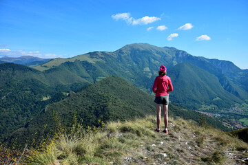 Fototapeta premium Woman standing on the summit of Corna Trentapassi overlooking Monte Guglielmo and other mountains. Lago d'Iseo, Brescia, Lombardy, Italy.