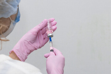 Close-up of the doctor's hands with a bottle and a vaccine, the vaccine is typed into a syringe. Medical concept vaccination subcutaneous injection treatment, prevention. On a white background.