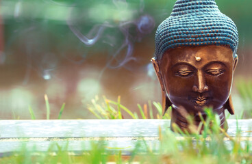 Buddha's head. Sculpture in the grass with smoke in the background.