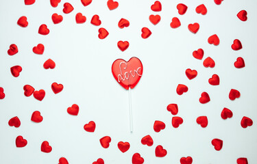 Fototapeta na wymiar Heart shaped lollipop with Love inscription. Flat lay composition for Valentine's Day, birthday, anniversary or wedding. With decorative hearts on white background.