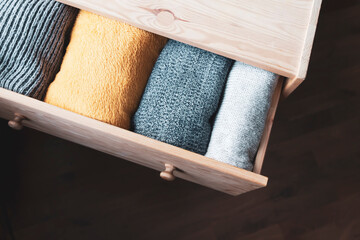 Open wooden dresser drawer with warm knitted woolen clothes. Home vertical storage. Wardrobe...
