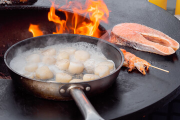 Process of cooking scallop meat, salmon, prawn on black brazier at summer outdoor food market: close up. Seafood, barbecue, gastronomy, cookery, street food concept