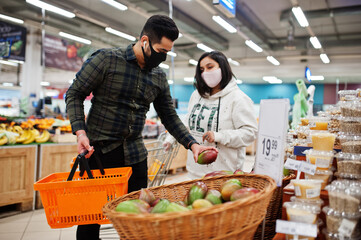 Asian couple wear in protective face mask shopping together in supermarket during pandemic. Taking mango fruit.
