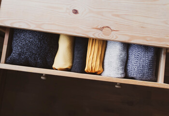 Open wooden dresser drawer with warm knitted woolen clothes. Home vertical storage. Wardrobe...
