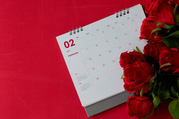 Top view, calendar of February with blurred red rose flower on the red background desk, the concept for Valentine's day on 14th February 2021. Close-up, Selective focus, Copy space for design or text.