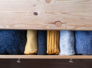 Open wooden dresser drawer with warm knitted woolen clothes. Home vertical storage. Wardrobe...