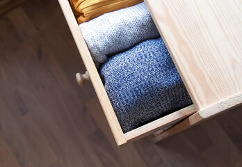 Open wooden dresser drawer with warm knitted woolen clothes. Home vertical storage. Wardrobe...