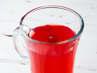 Selective focus on cranberries floating in a fresh drink in a glass cup. In the background there is a blurred bright white wooden background. Fresh ripe berries are a source of vitamins. Copy space.